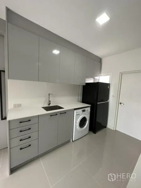 Townhouse for rent in Bang Phli, Samut Prakan - Kitchen counter with sink, overhead cabinets, washer and fridge.