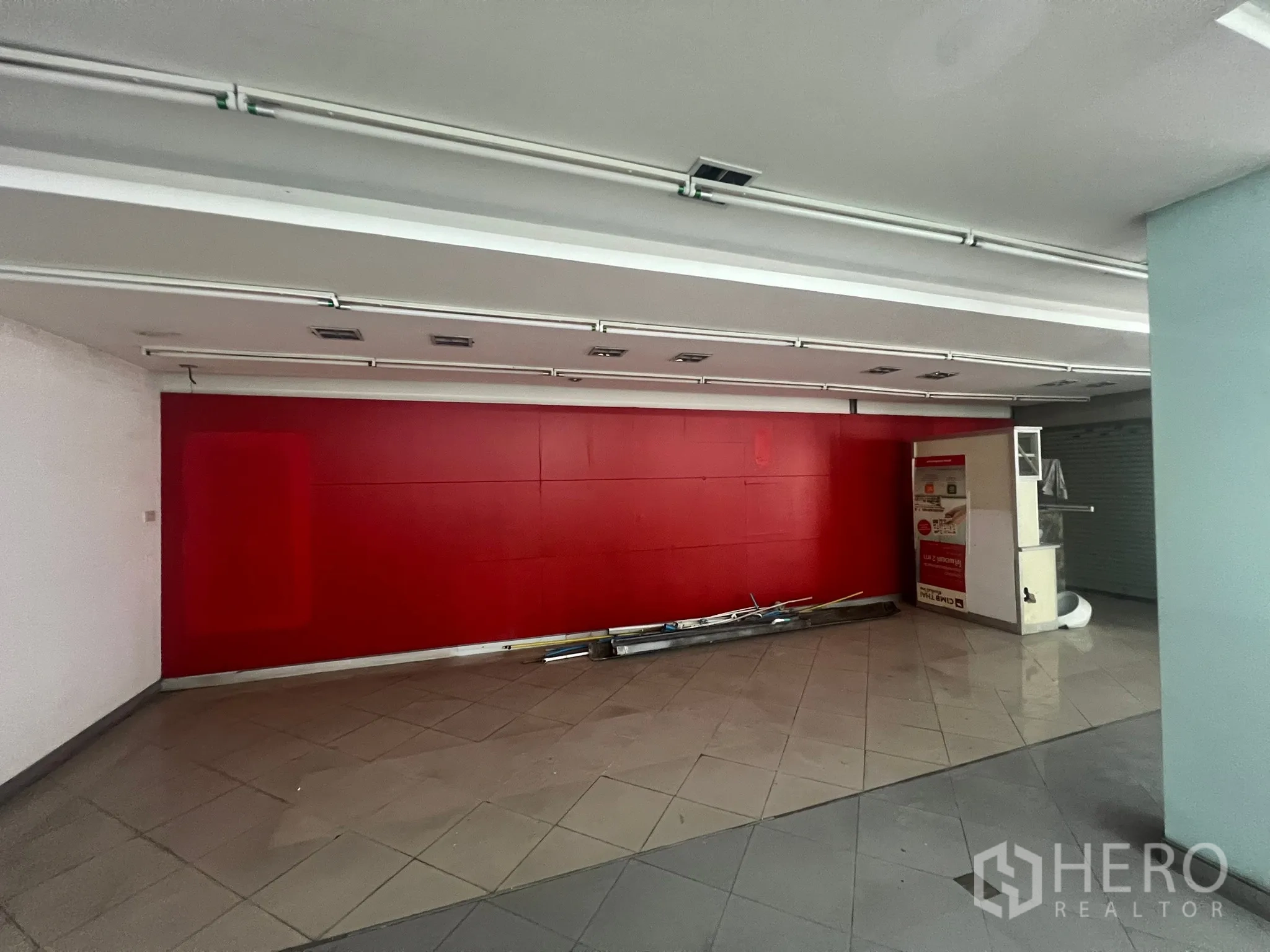 店屋 出租在Watthana, Bangkok - 开阔店面内红色背景墙特写，吊顶灯带与瓷砖地面清晰可见。