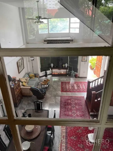Home Office for rent in Bang Rak, Bangkok - View from the mezzanine into the high-ceiling living area with red rugs and large windows.