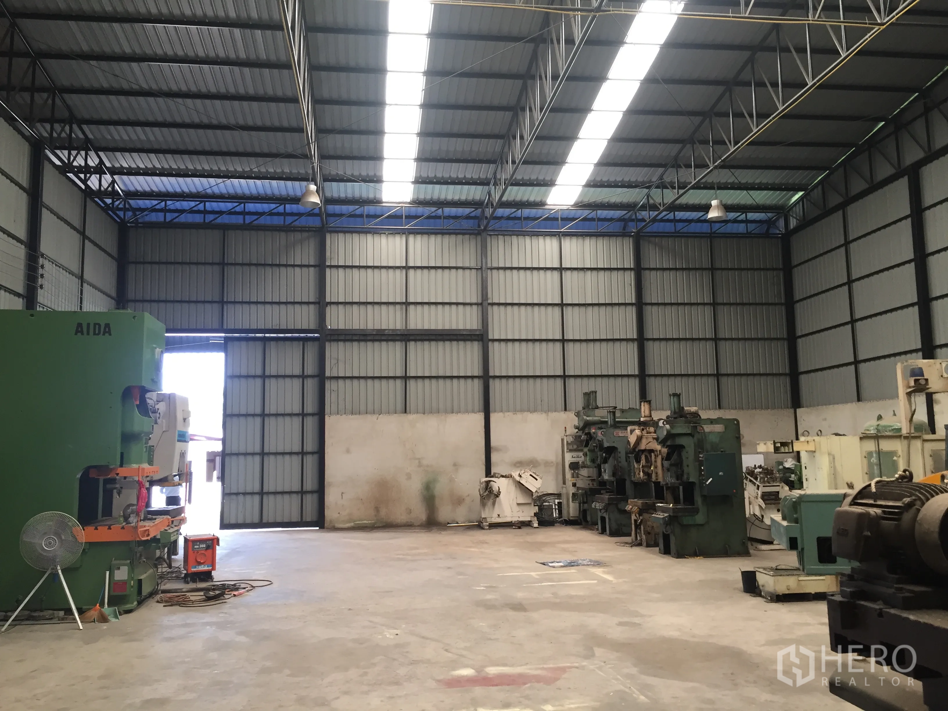 Warehouse for rent in Lat Krabang, Bangkok - Spacious warehouse hall with large sliding door, overhead lights, and storage area.