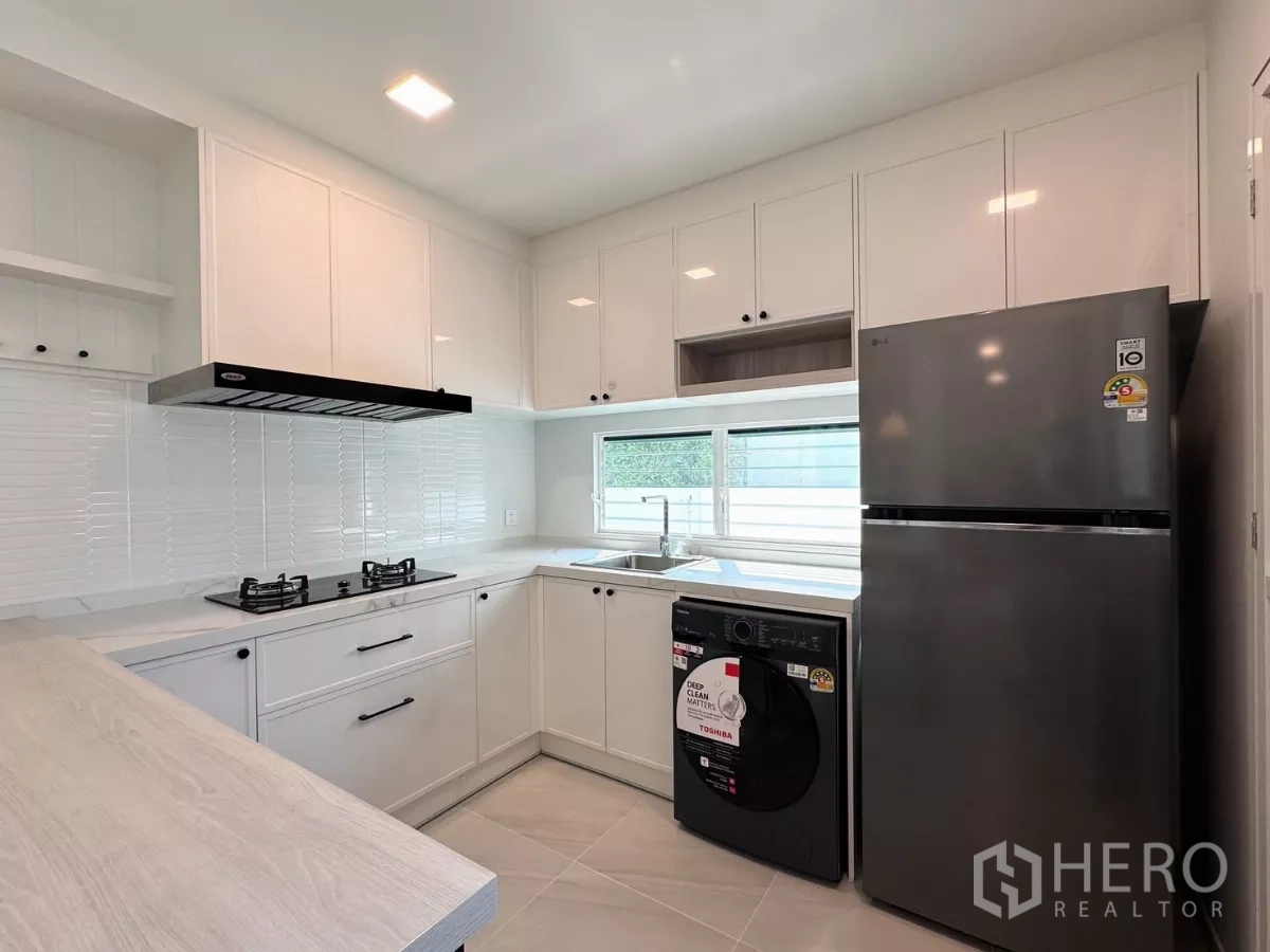 Detached House for rent in Bang Phli, Samut Prakan - White L-shaped kitchen with refrigerator and washing machine under the window.