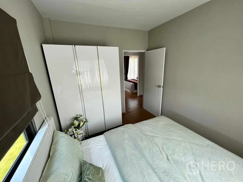 Townhouse for sale in Sai Mai, Bangkok - Compact bedroom with white wardrobe, bed, light grey walls, and a doorway to an adjoining room.