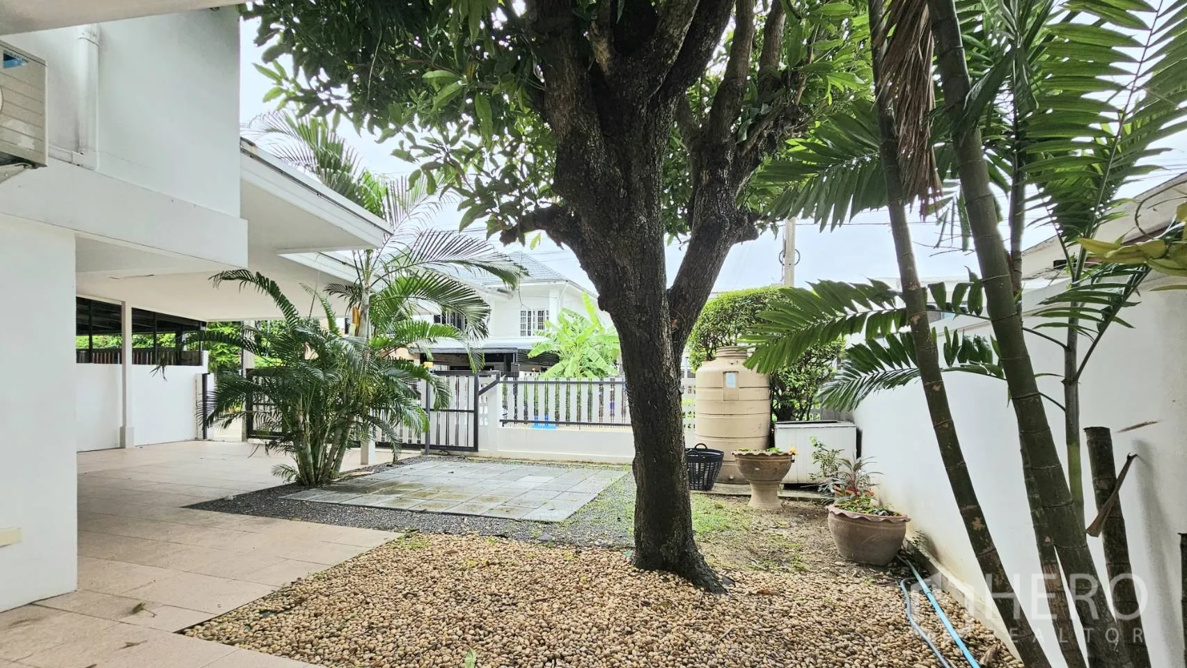 Detached House for rent in Saphan Sung, Bangkok - Shaded garden with mature tree, pebbled ground, and paved area near the gate.