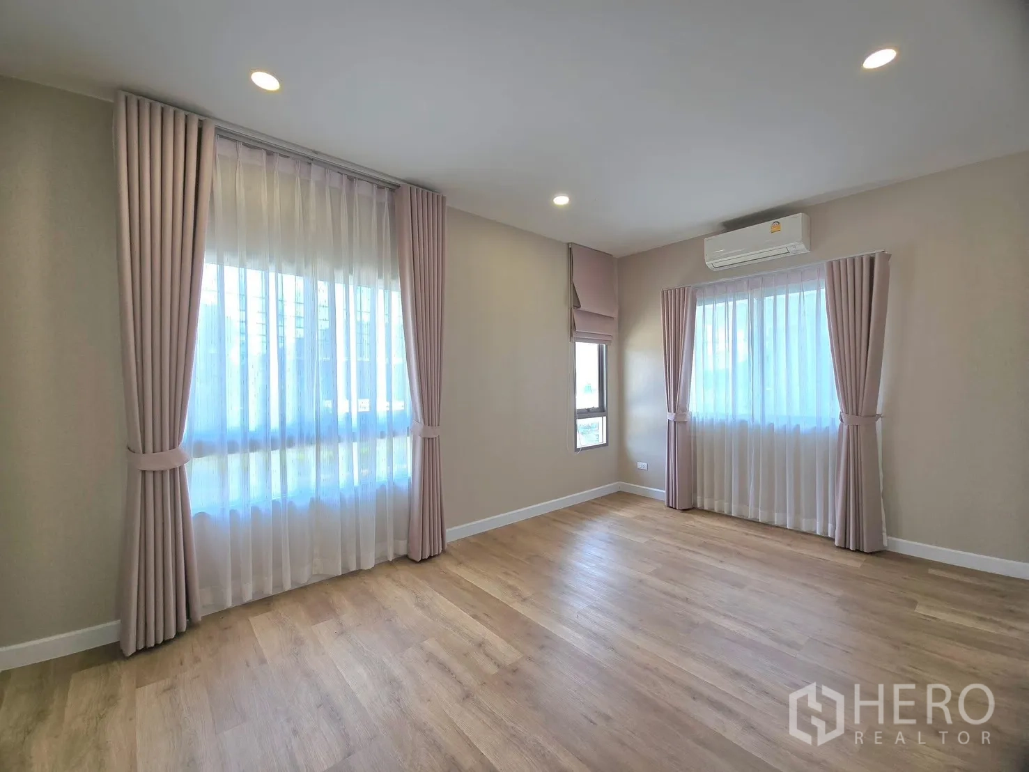 Detached House for rent in Lat Krabang, Bangkok - Corner bedroom with two large curtained windows and an air conditioner.