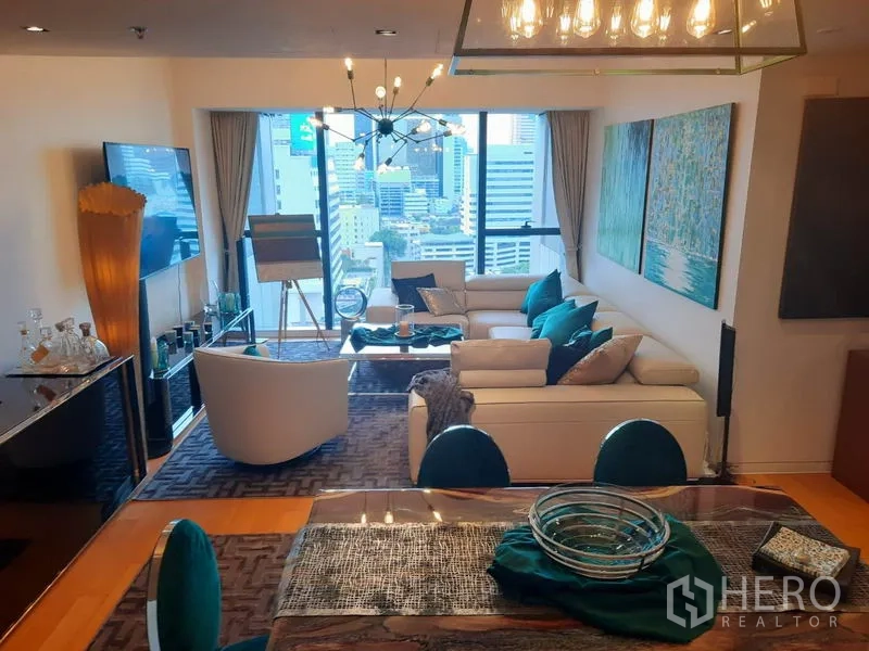Condominium for rent or sale in Sathon, Bangkok - Stylish living room with chandelier, white sofas and floor‑to‑ceiling windows overlooking the Bangkok skyline.