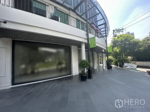 Office Space for rent in Khlong Toei, Bangkok - Wide tiled walkway with potted plants along a curved glass facade of a low-rise commercial building.
