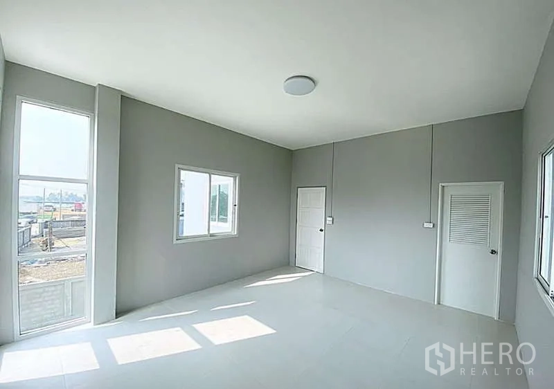 Warehouse for sale in Pathum Thani - Bright office room with large windows, grey walls and tiled floors overlooking the yard.