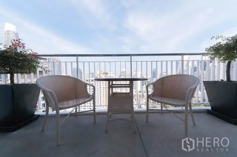 公寓 出租在Pathum Wan, Bangkok - 高层阳台，两把藤椅与小桌，俯瞰曼谷天际线。