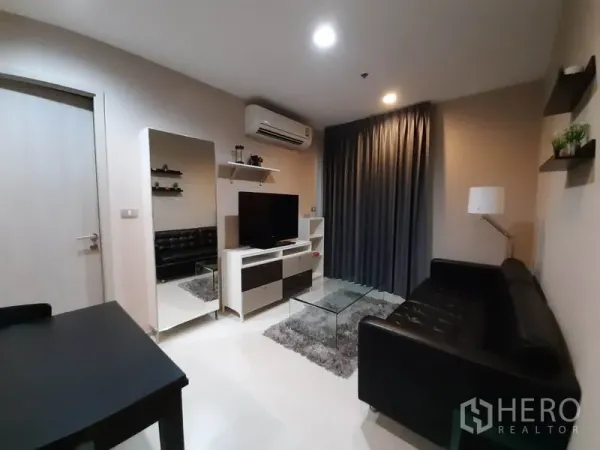 คอนโด ให้เช่าหรือขายในKhlong Toei, Bangkok - ห้องนั่งเล่นอบอุ่น โซฟาหนังสีดำ ชั้นวางทีวี กระจกเงาบานใหญ่ และโต๊ะกลางกระจก พร้อมผ้าม่านทึบสีเทา