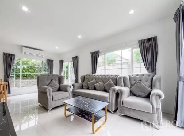 独立式住宅 出租在Chom Thong, Bangkok - 明亮客厅，灰色绒面沙发组合、仿石纹茶几与大窗户。