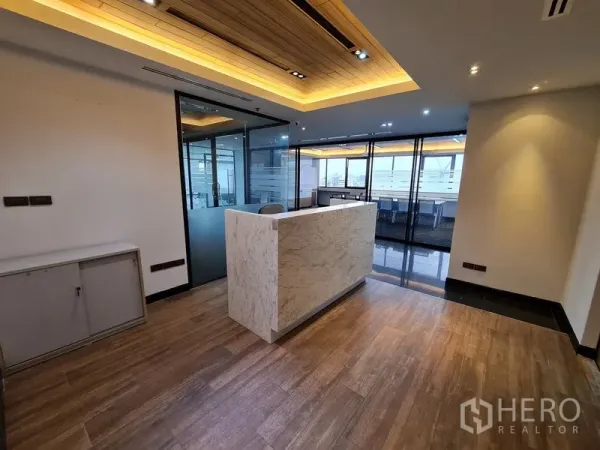 办公空间 出租在Bang Rak, Bangkok - 现代接待区，石纹前台、木地板与玻璃隔间，暖色筒灯照明。