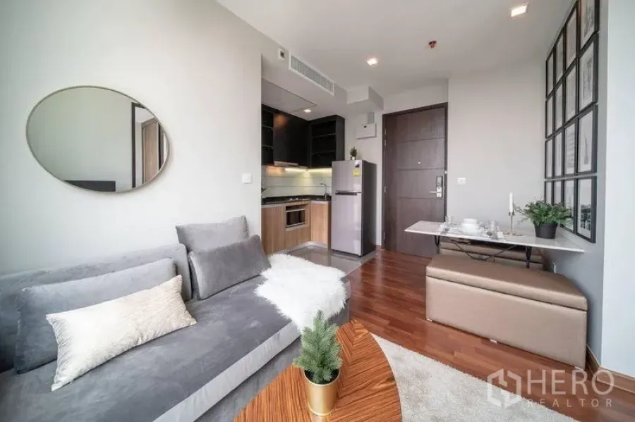 Condominium for rent in Ratchathewi, Bangkok - Living area facing the entry and kitchenette, featuring gray sofa, marble dining table, and wood flooring.