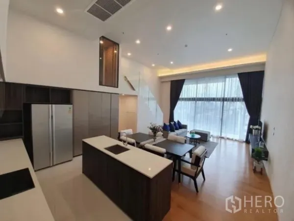 Condominium for rent in Watthana, Bangkok - Sleek kitchen with island, induction hob, tall cabinets and double-door fridge opening to a bright living space.