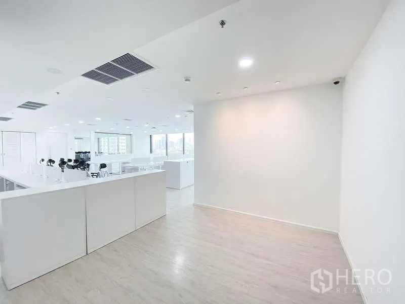 办公空间 出租在Din Daeng, Bangkok - 明亮的开放式办公室，浅色木地板与筒灯照明，前区墙面连接到靠近大窗的工位区。