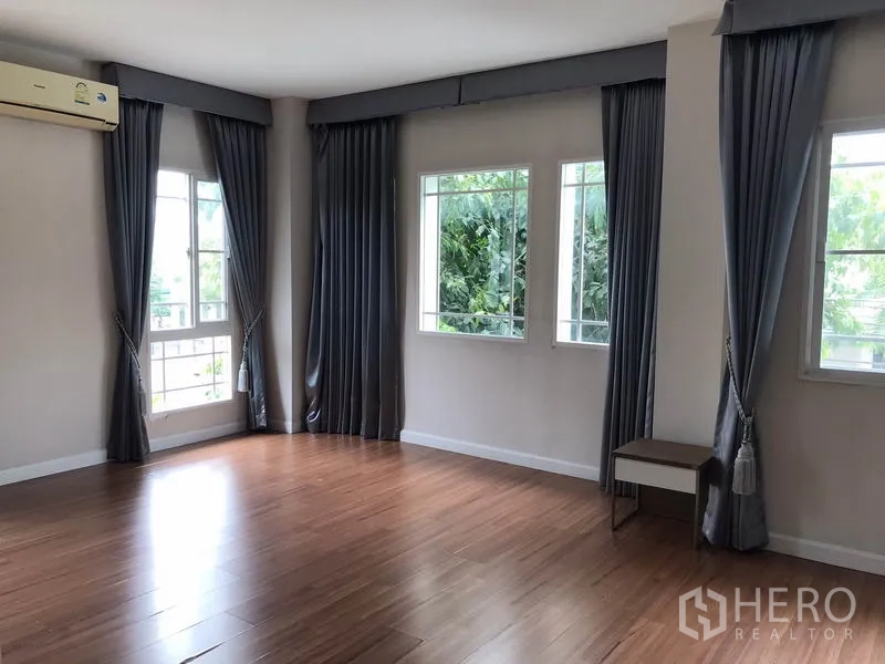 Detached House for rent in Khlong Sam Wa, Bangkok - Spacious bedroom with wood floors, grey curtains and multiple windows.