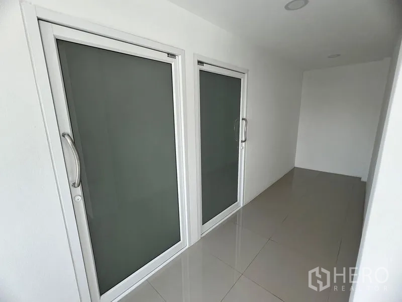 零售空间 出租在Huai Khwang, Bangkok - 现代商铺走廊，一侧有两扇磨砂玻璃门与亮面地砖。