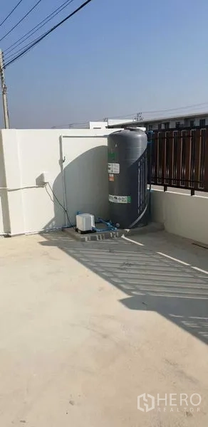 Factory for rent in Lam Luk Ka, Pathum Thani - Outdoor utility area with water tank and pump on a concrete terrace beside the fence.