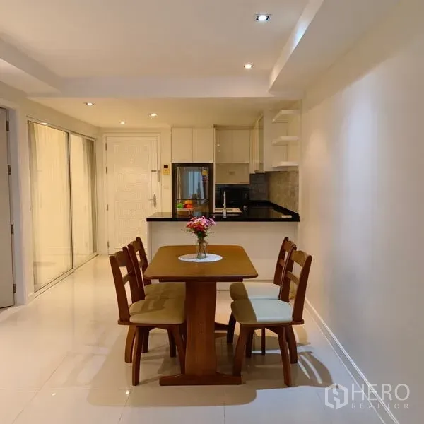Condominium for rent in Watthana, Bangkok - Open-plan dining area and U-shaped kitchen with white cabinets and black granite countertop in an Ekkamai condominium.