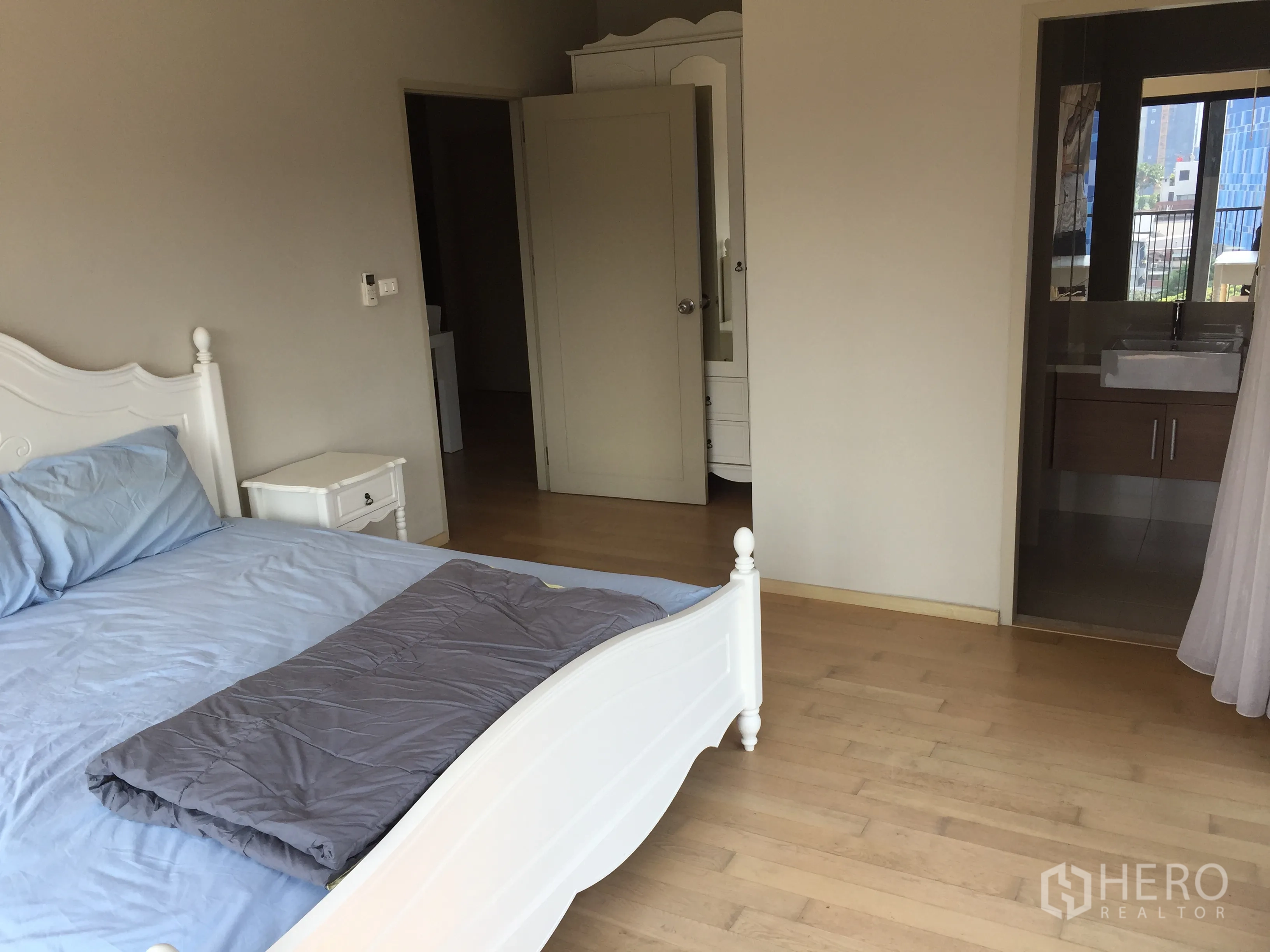 Condominium for rent or sale in Watthana, Bangkok - Spacious master bedroom with wood floors and an ensuite bathroom entrance in a modern Bangkok condo.
