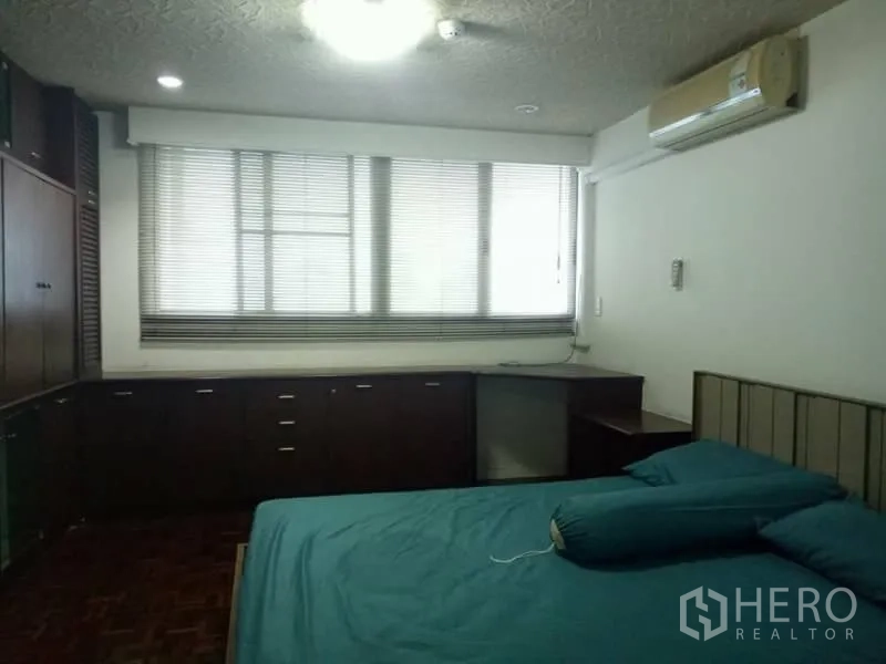 Condominium for rent in Watthana, Bangkok - Second bedroom with dark wood built-ins, corner desk, window blinds and wall-mounted air conditioner.