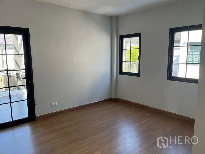 Detached House for rent in Bang Phli, Samut Prakan - Bright corner bedroom with wood floors, two windows and a door to the balcony.