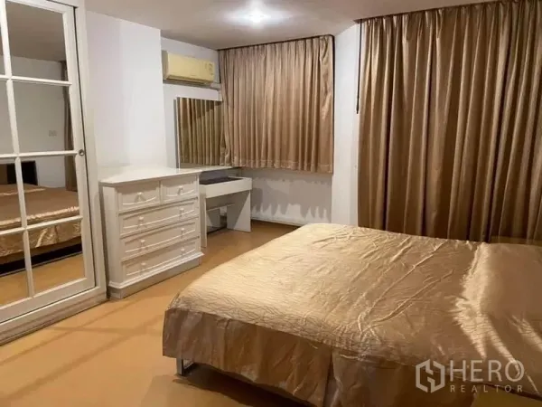 Condominium for rent or sale in Watthana, Bangkok - Primary bedroom with gold curtains, mirrored wardrobe, dresser, and vanity desk.