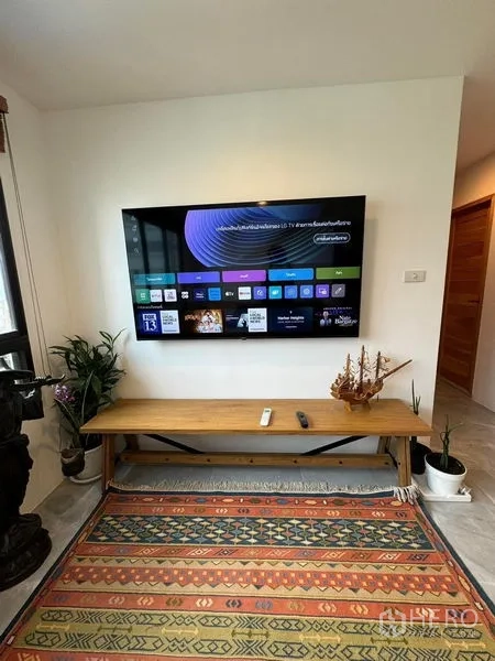 公寓 出租或出售 - 客厅内壁挂智能电视，上方木长凳与绿植装饰。