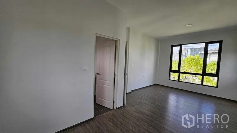 Detached House for sale in Samut Prakan - Bedroom with ensuite door and big window overlooking the neighborhood greenery.