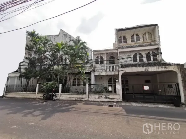 Detached House for rent in Khlong Toei, Bangkok - Street view of a multi-level detached house with arched windows, balconies, gated carport and tall palm trees in Watthana, Bangkok.