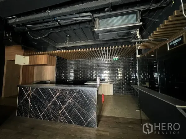 零售空间 出租在Din Daeng, Bangkok - 深色吧台区，黑色地铁砖、石材台面与木格栅吊顶。