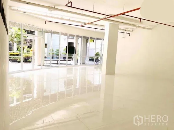 办公空间 出租在Khlong Toei, Bangkok - 宽敞白色室内空间，中央立柱，地面光洁，宽幅玻璃门面与玻璃门引入充足自然光。