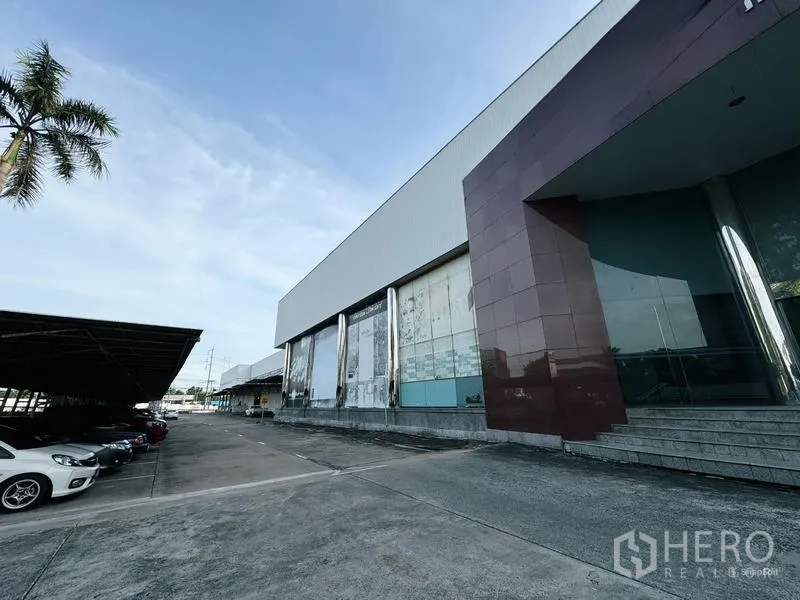 展厅 出租在Min Buri, Bangkok - 长条玻璃立面，配有有顶停车区和棕榈树车道。