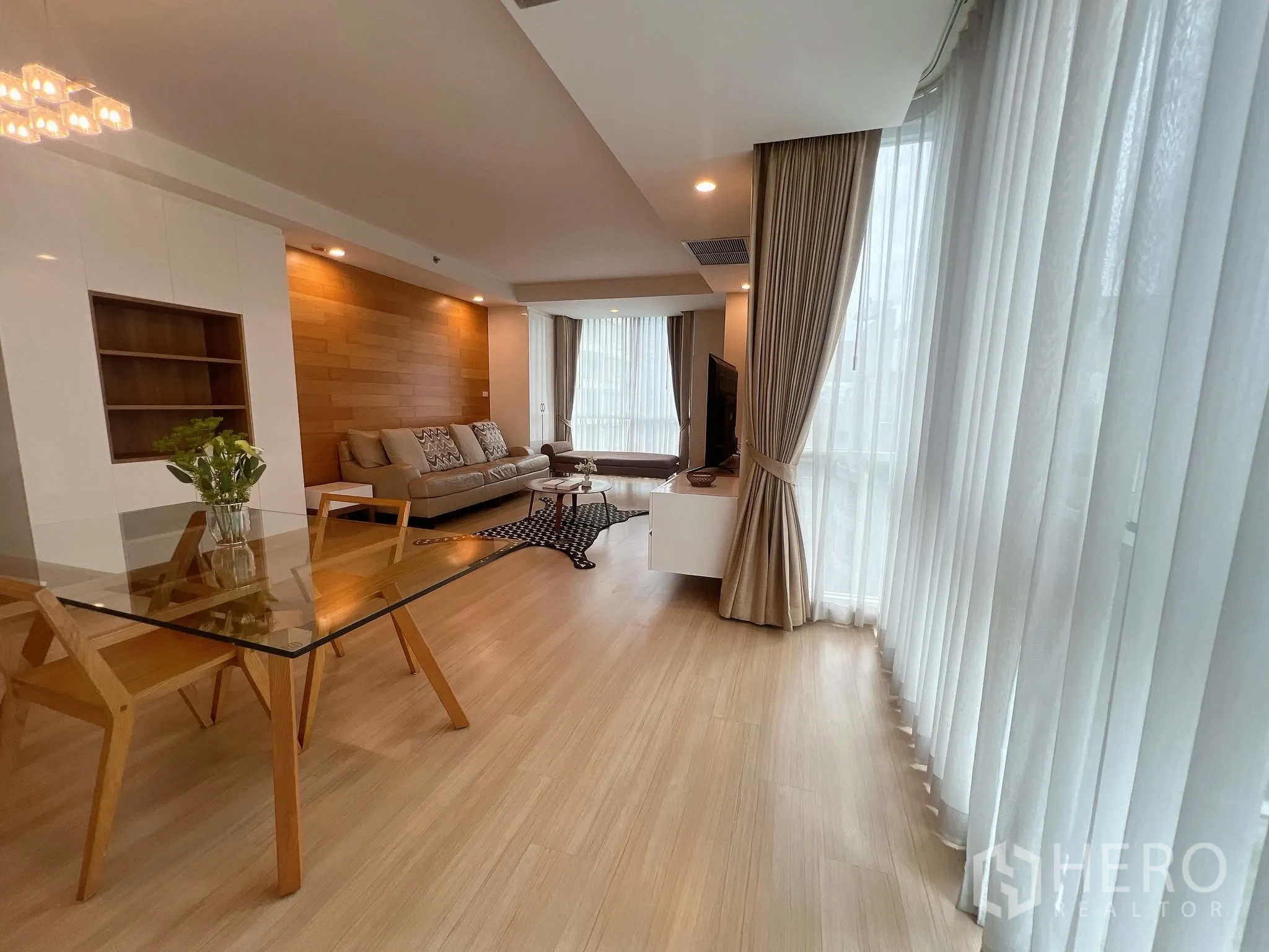คอนโด for rent in Pathum Wan, Bangkok - ห้องนั่งเล่นและรับประทานอาหารสว่าง โต๊ะกระจก โซฟาสีเบจ พื้นไม้ และหน้าต่างสูงจรดเพดานพร้อมผ้าม่าน