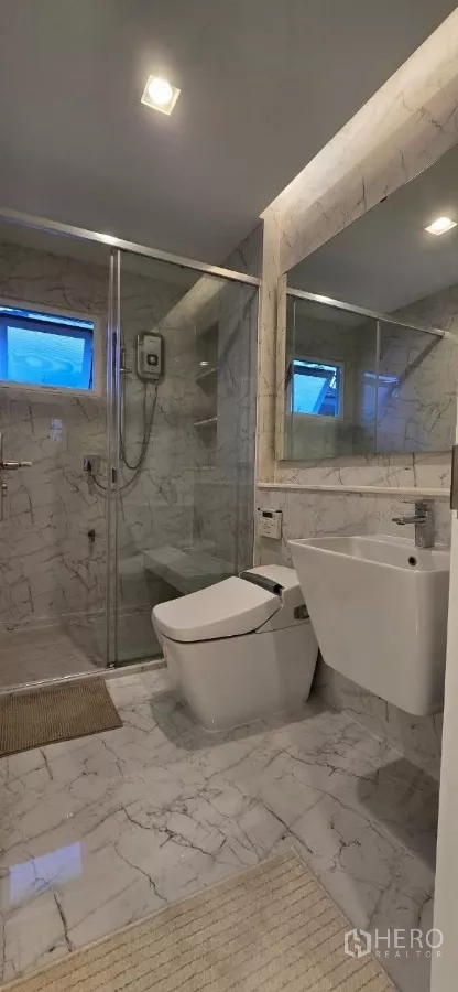 Detached House for rent in Samut Prakan - Marble-tiled bathroom featuring a glass shower and wall-hung basin.
