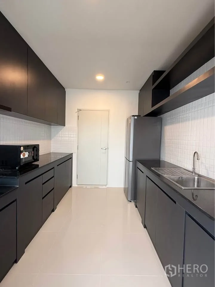 Detached House for rent in Bang Phli, Samut Prakan - Sleek galley kitchen with black cabinetry, sink, and refrigerator.
