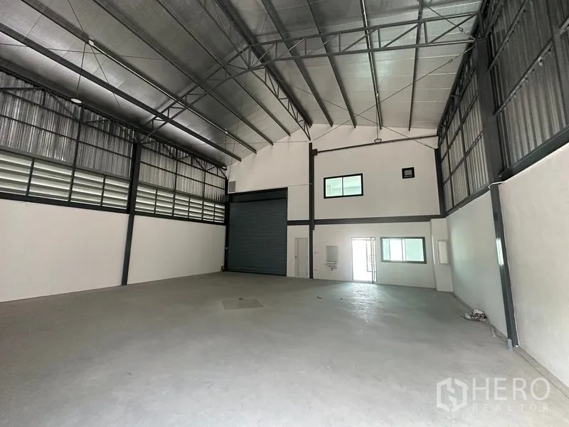 工厂 出租或出售在Bang Bua Thong, Nonthaburi - 仓库内部朝向卷闸门，可见办公室窗与洗手池。