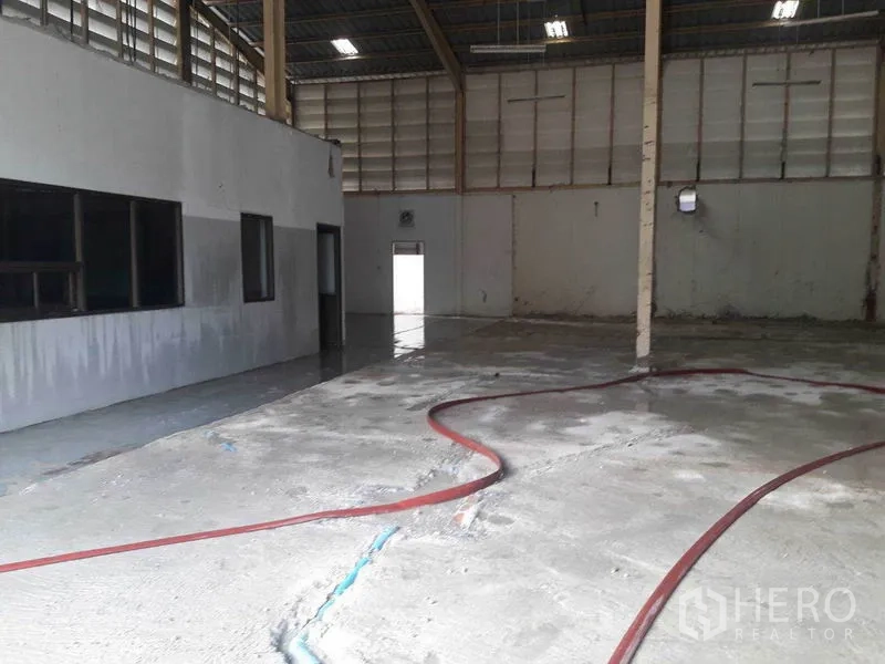 Warehouse for rent in Bang Sue, Bangkok - Warehouse hall with office rooms and water hose on polished concrete floor.