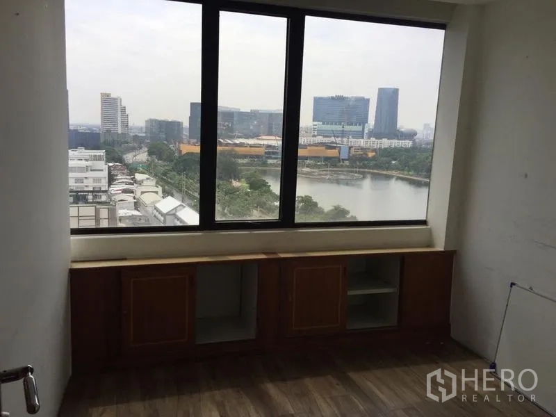 Office Space for sale in Watthana, Bangkok - Bright room with large window overlooking a lake and towers, base cabinets below.