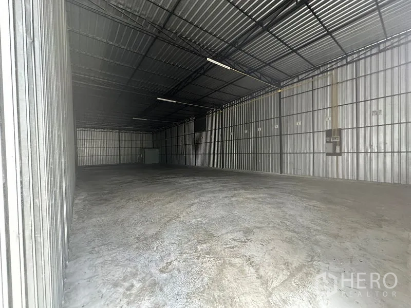 Warehouse for rent in Wang Thonglang, Bangkok - Front view of the warehouse interior showing a large column-free space, ceiling lights, and an electrical panel on the side wall.