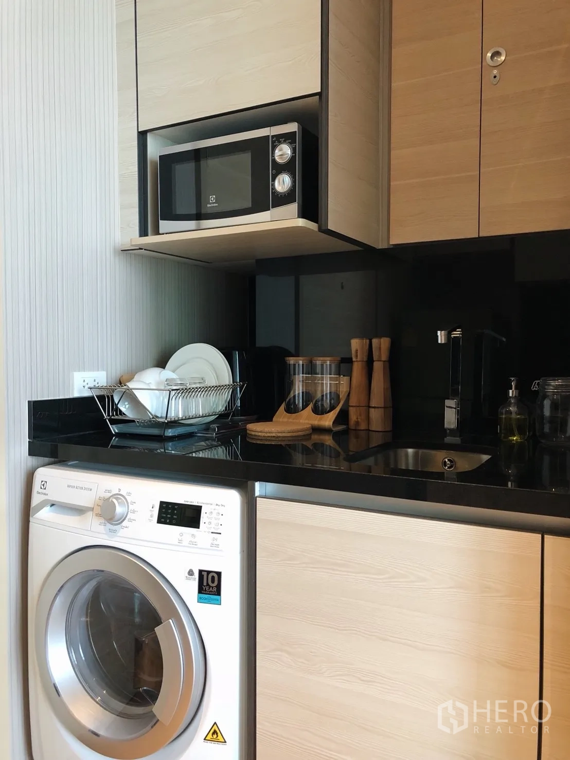 Condominium for rent in Khlong Toei, Bangkok - Built-in kitchenette featuring microwave, black countertop, sink, and front-loading washer.