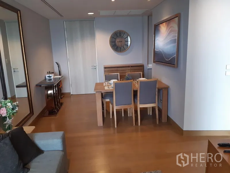 Condominium for rent in Khlong Toei, Bangkok - Cozy dining corner with wooden table, upholstered chairs, wall art and a large mirror.