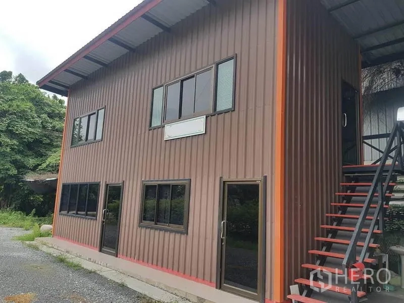 Warehouse for rent in Sai Noi, Nonthaburi - Two-storey metal-clad office building beside the warehouse with exterior stairs.