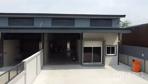 货栈 出租在Bang Bua Thong, Nonthaburi - 仓库正立面，超宽卷闸、办公室窗户、通风百叶与宽阔前院。