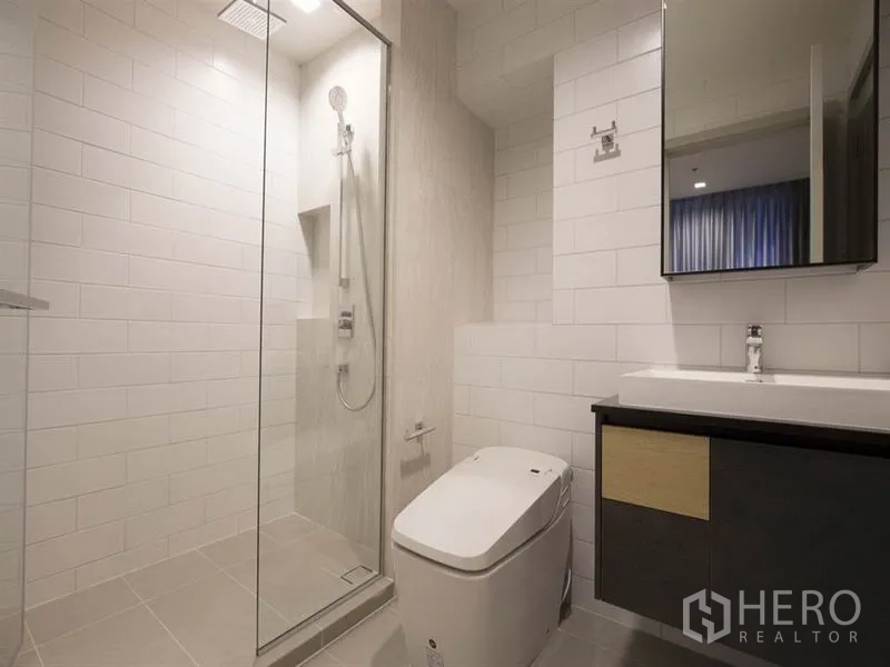 Condominium for rent in Chatuchak, Bangkok - Modern bathroom featuring glass shower with rain head, vanity, and toilet.