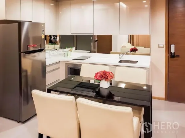 公寓 出租在Bang Rak, Bangkok - 现代厨房配白色橱柜、镜面防溅板、电磁炉与不锈钢冰箱，四人餐桌。