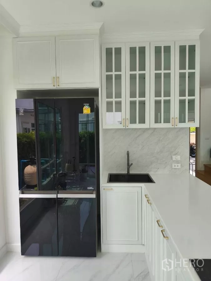Detached House for rent in Bang Phli, Samut Prakan - Close-up of kitchen sink with black faucet, marble backsplash, and glass-door upper cabinets.