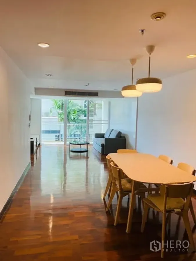 Condominium for rent in Watthana, Bangkok - Open-plan dining and living area with wooden floors, pendant lights, and sliding glass doors to a balcony.