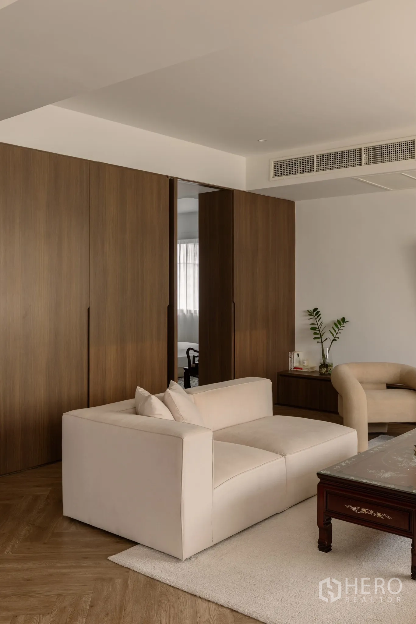 Condominium for sale in Khlong Toei, Bangkok - Close view of living area showing cream sofa, wood panel storage wall and indoor plant.