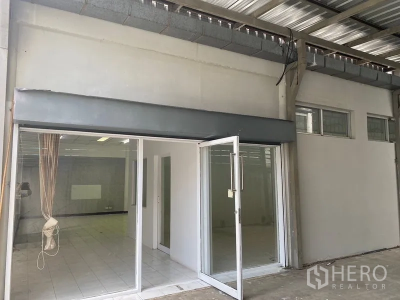 Warehouse for rent in Chatuchak, Bangkok - Glass‑fronted office beneath a metal canopy next to high windows.