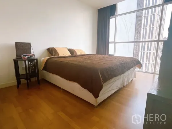 Condominium for rent or sale in Sathon, Bangkok - Bright bedroom with wooden flooring, large bed and floor-to-ceiling windows overlooking the city.